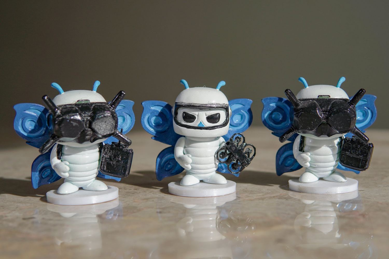 Tres figuras impresas en 3D de Hélix, la mascota de Space Print: con gafas FPV y radio, con casco y con un dron